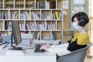 Girl with protective mask and headphones working on computer