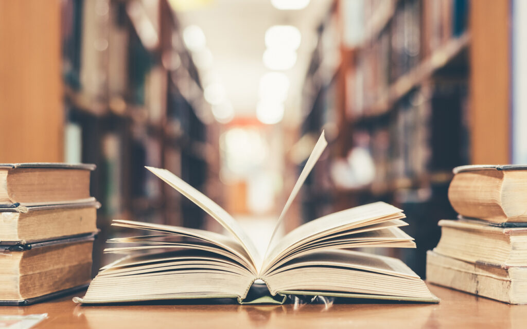 Book in library with old open textbook, stack piles of literature text archive on reading desk