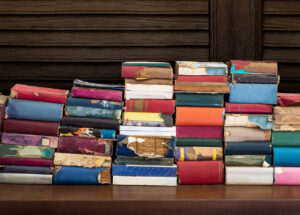 Heap up of old and damaged book on wooden table with wooden wall background