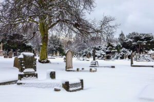 Cemetery winter with snow covered graveyard tombstone cross after a blizzard snowfall