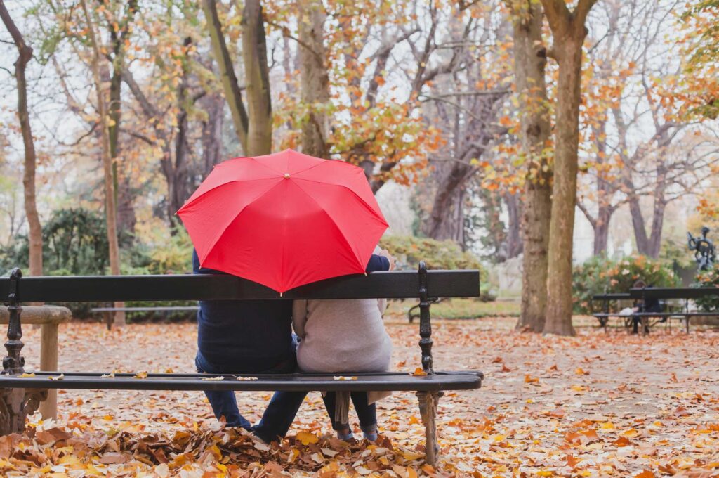 Two people sitting on a bench under and umbrella